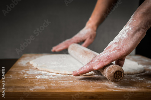 the cook rolls out the dough with a rolling pin. hands close up