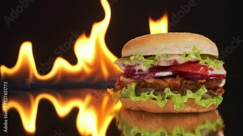 An appetizing and tasty chicken burger on a mirror table, a fire burns in the background.