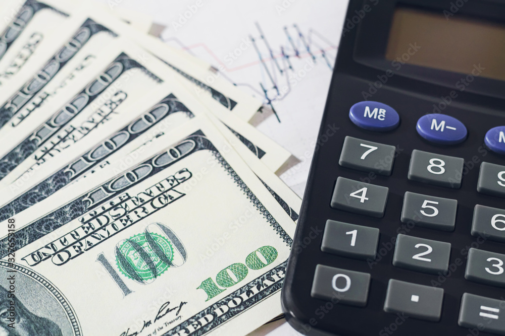 Dollar banknotes and calculator over blurred trading graph. Finance, accounting or saving concept. Dollar banknotes and calculator over blurred trading graph. Finance, accounting or saving concept.