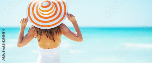 Foto Young woman in hat standing on beach. rear view