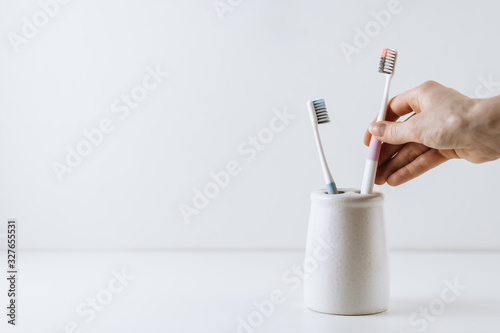 Hand takes a toothbrush from a white cup. One brush stands out. White background with copy space. oral care concept