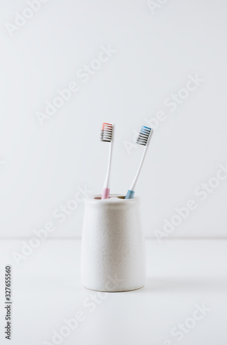 blue and pink toothbrushes in a white cup  isolated on white background