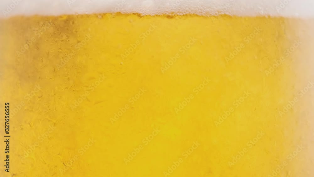 Light cold beer is poured into a rotating beer glass, beer in a glass with water drops, macro 4K UHD video. Light cold beer is poured into a rotating beer glass, beer in a glass with water drops, macro 4K UHD video.