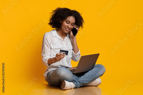 Happy afro woman using credit card and laptop, talking on phone