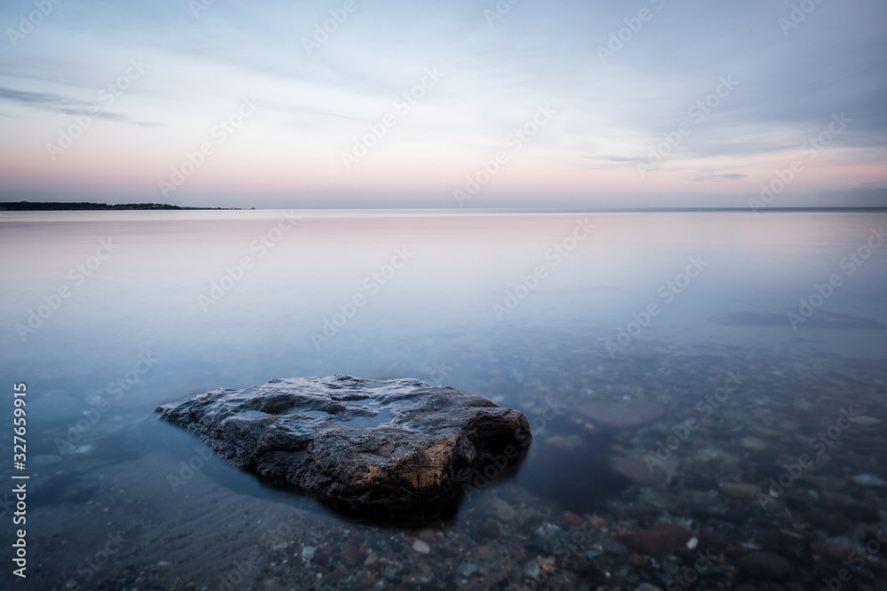 Calm romantic peaceful morning at coast of baltic sea with rock in foreground and cloudy sky in background, Sehlendorf, Schleswig-Holstein, Northern Germany 