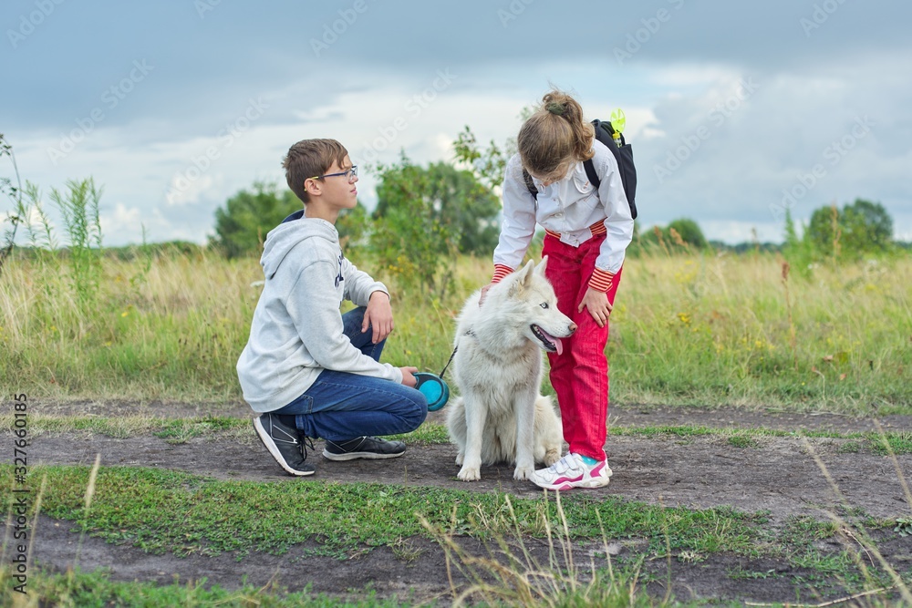 Children walking with white dog in meadow on autumn day Children walking with white dog in meadow on autumn day