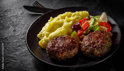 burger with mashed potatoes and vegetables salad on a black plate on Dark grey black slate background photo