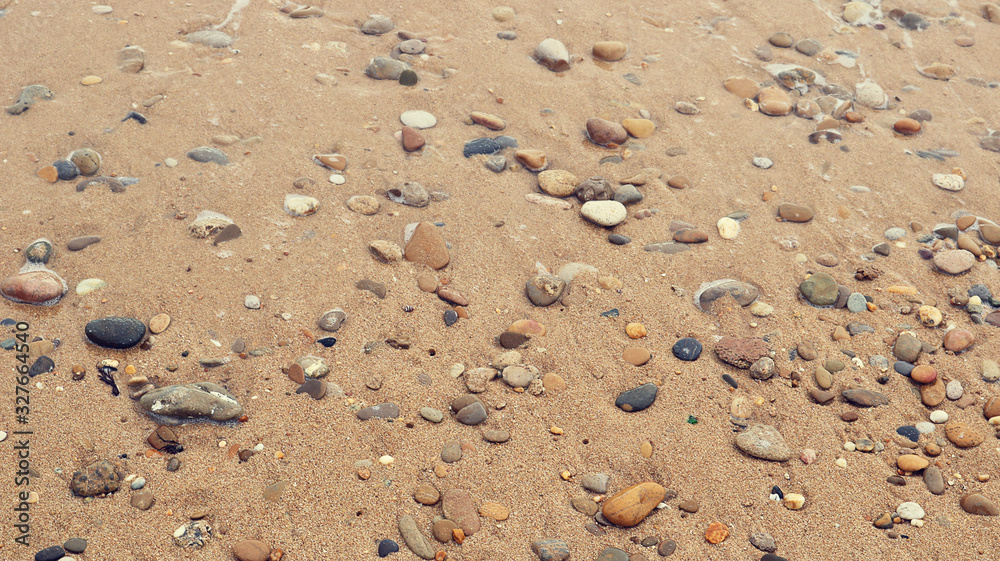 texture of wet sand of a beach with round colorful stones next to the sea