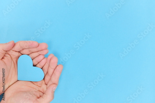 Blue heart shape cutout on hands in blue background. Top view, kindness and charity concept. photo