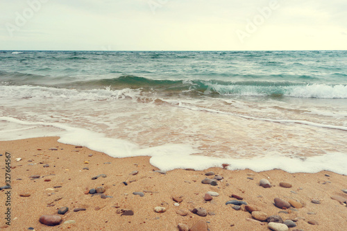 Fototapeta Naklejka Na Ścianę i Meble -  soft wave of the atlantic ocean with foam over a beach with sand and stones - calm, cloudy and lonely afternoon wallpaper