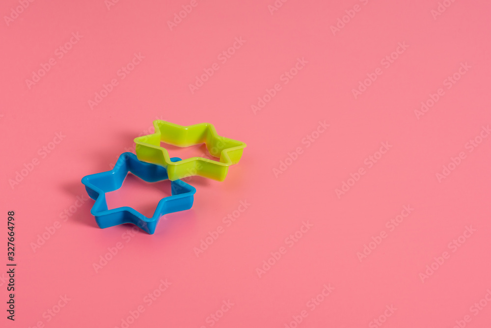 Two plastic molds of blue and green colors for making cookies in the shape of a star on a pink background. Culinary concept. Flat lay with copyspace. Two plastic molds of blue and green colors for making cookies in the shape of a star on a pink background. Culinary concept. Flat lay with copyspace.