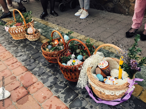 Easter baskets with stylish painted eggs, easter cake, ham,beets, butter, candle with boxwood branches for sanctify at church on background of people feet. Easter food for blessing photo