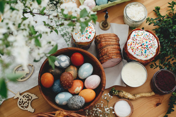 Easter food flat lay. Easter eggs natural dyed, easter bread, ham, beets, butter, green branches and flowers on rustic wooden table. Traditional Easter Food for breakfast