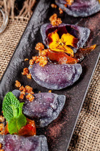 Ukrainian cuisine in the European style. Sweet dumplings with cherries, candied orange and edible flowers. Beautiful serving in the restaurant. background image, copy space text