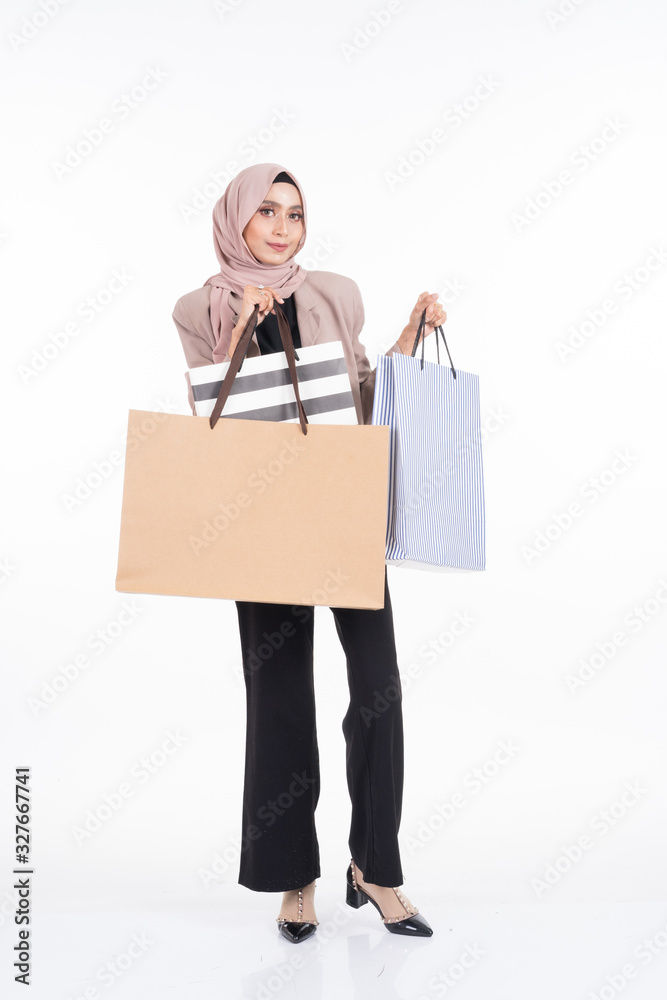 A beautiful Asian Muslim woman wearing officewear and hijab poses with shopping bags isolated on white background. Full length portrait for business and commerce concepts. A beautiful Asian Muslim woman wearing officewear and hijab poses with shopping bags isolated on white background. Full length portrait for business and commerce concepts.