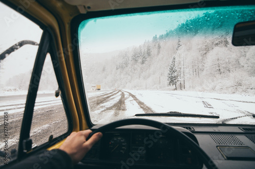 View from the driver seat over the snowy dirt road with winter forest on background in Carpathian mountains, Ukraine