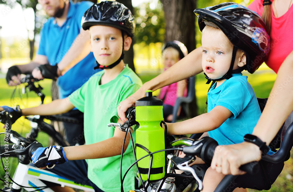 Obraz premium a small child a boy in equipment and a helmet sits in a children's Bicycle seat near his parents against the background of the Park and nature