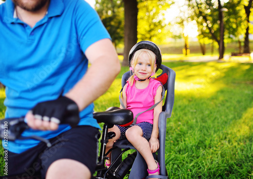 a man dad in a sports uniform carries a little girl daughter on a Bicycle in a children's Bicycle seat.