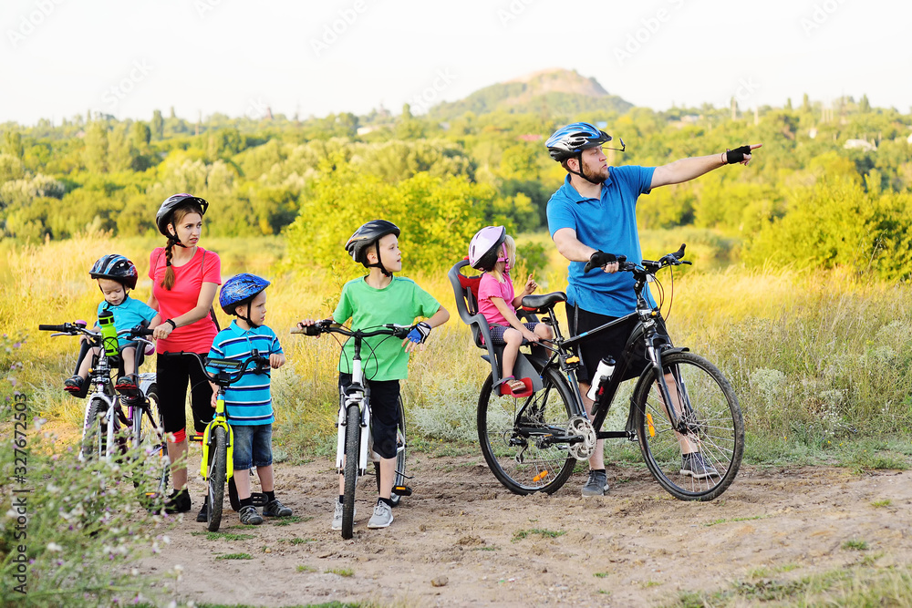 a group of people on bicycles - two adults and four young children in Bicycle gear and helmets against the background of trees, Park and green grass. Family and active lifestyle.