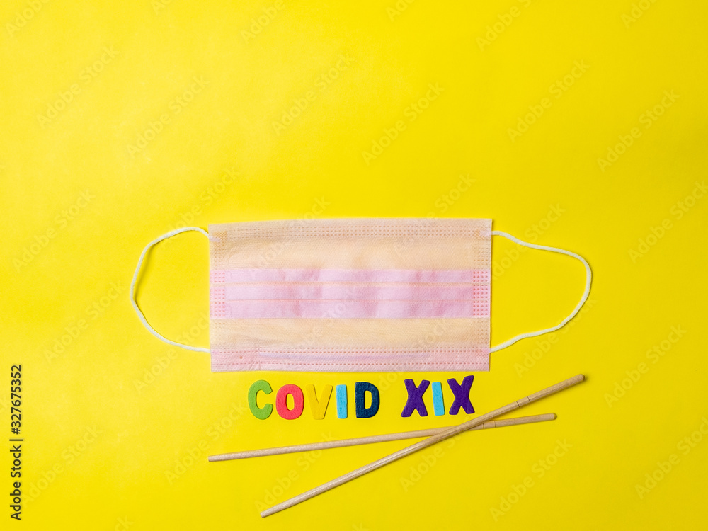 Pink medical mask on a yellow background and Asian chopsticks in the shape of the letter V. Disease as a treat from Asia