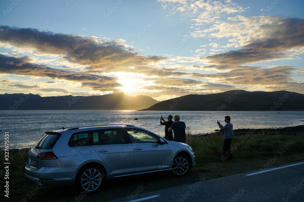 Three men having a stop to photograph sunset on road trip at Arctic Senja Tromso Norway beautiful fjord car standing by