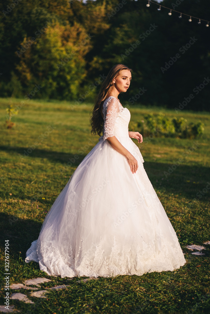 Beautiful young woman in a white wedding dress and black boots at sunset is photographed.