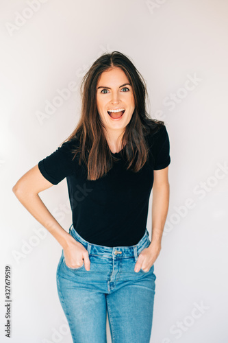 Indoor portrait of beautiful laughing woman, wearing black t-shirt and high waist jeans, posing on white background