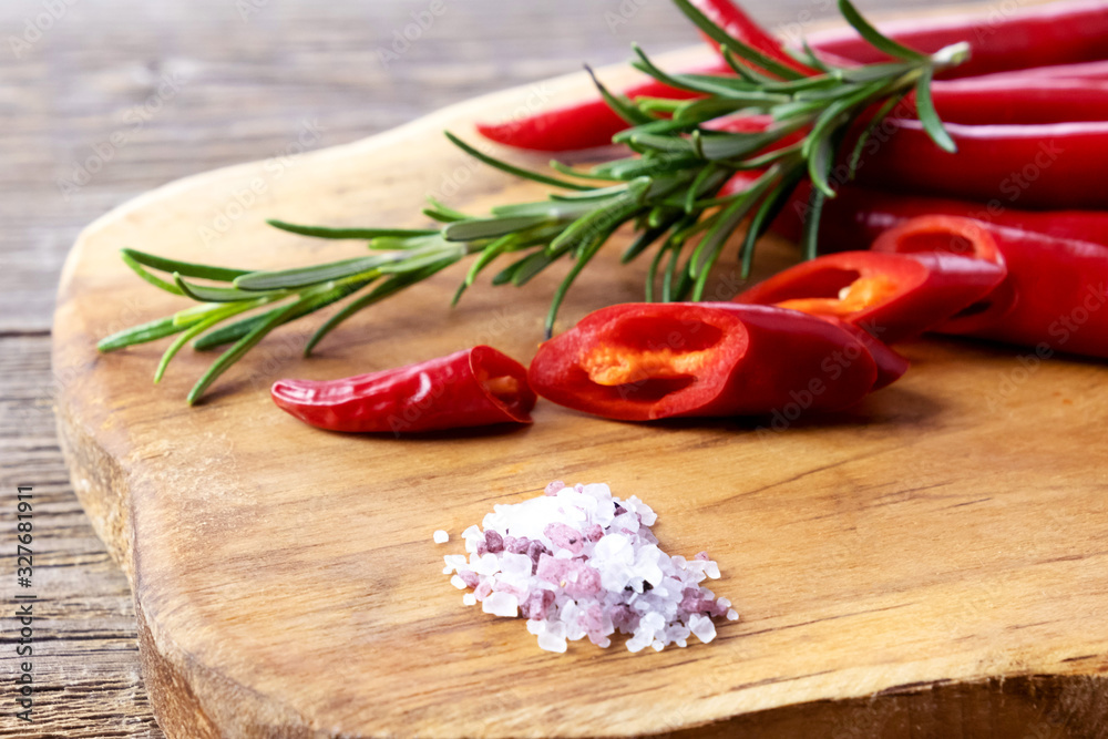 Red organic chili peppers on a wooden board. Nearby lies sea salt and a sprig of rosemary. Hot seasoning. Place for text Red organic chili peppers on a wooden board. Nearby lies sea salt and a sprig of rosemary. Hot seasoning. Place for text