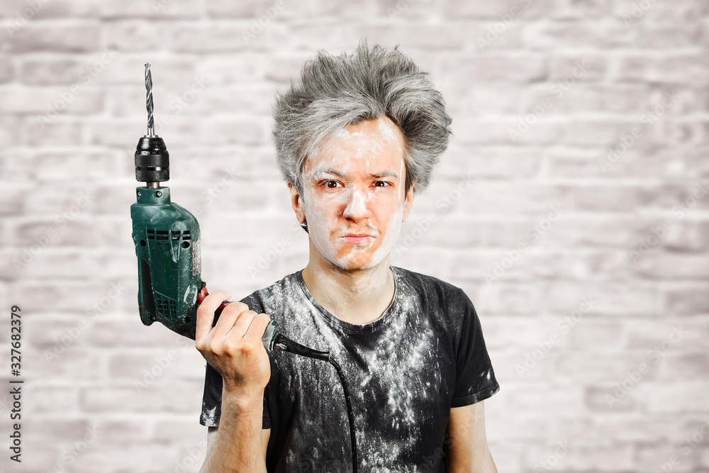 Dirty young builder guy in plaster is hold a green drill perforator on at home during repairs on brick wall background Dirty young builder guy in plaster is hold a green drill perforator on at home during repairs on brick wall background