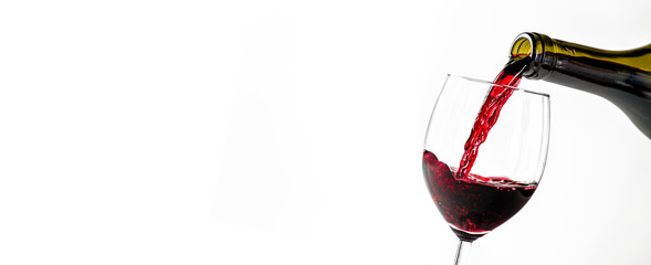 Pouring glass of red wine from a bottle in wide banner shape or copy space for text.. White background or isolated.
