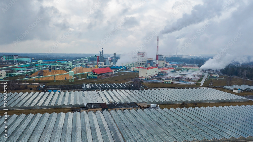 Aerial view greenhouse on the background of smoke from the pipes of the pulp mill. Ecological problem concept.