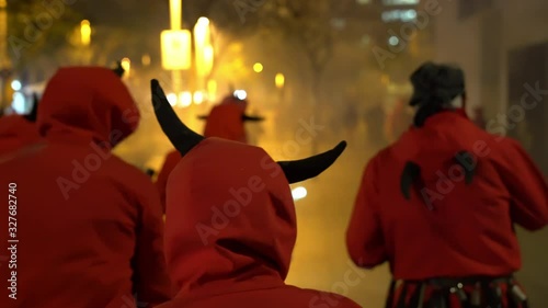 people in devil costumes with horns watch a fire show and go into the distance photo