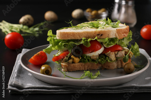Sandwich with chicken, cherry tomatoes, quail eggs, olives and microgreens against a dark background