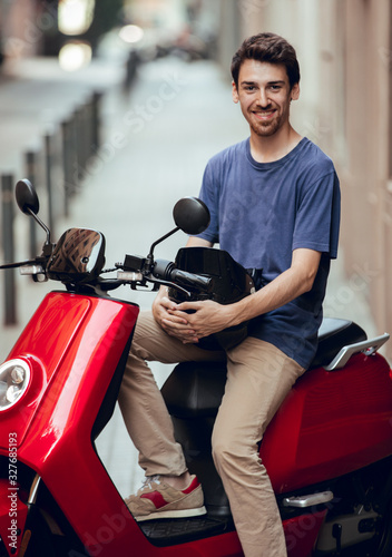 Close up of Smiling Biker boy with black helmet sitting on red motorcycle