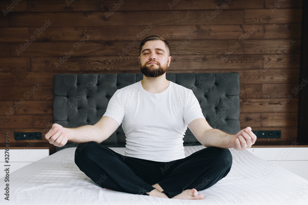 Fototapeta premium Handsome caucasian man meditating and practicing mindfulness on his bed in bedroom