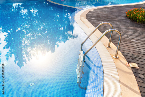 Steps into the pool with handrails in water reflex sun. For tourists.