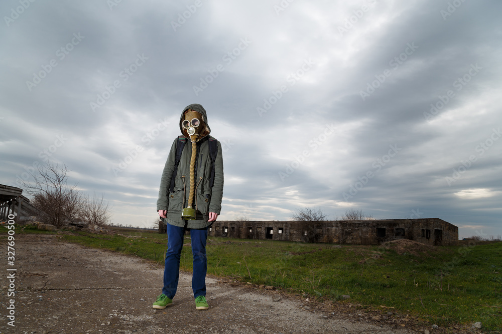 Human in gas mask standing among ruins and dramatic sky background. Enviromental pollution, ecology disaster, radiation, biological hazard concept.