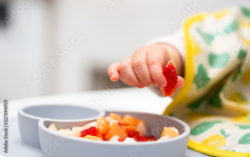 Stampa su tela Macro Close up of Baby Hand with a Piece of Fruits Sitting in Child's Chair Kid