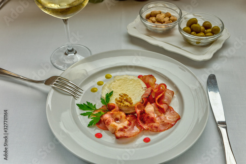 Warm goat cheese with honey and bacon served on a white dish, served with a glass of delicate white wine