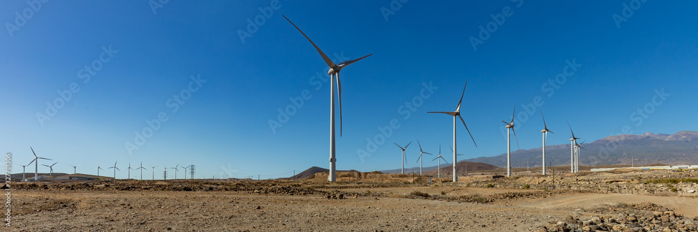 Super wide panorama of Wind power stations. A row of turbines near the seashore. Wind farm eco field. Eolic park with blue sky in background. Green, ecological and power energy generation concept Super wide panorama of Wind power stations. A row of turbines near the seashore. Wind farm eco field. Eolic park with blue sky in background. Green, ecological and power energy generation concept