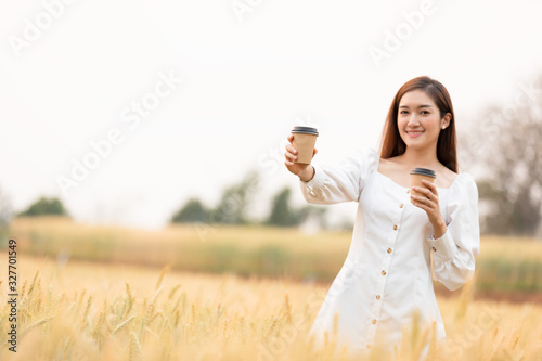 Young woman holding takeaway coffee cup standing outdoors at barley field land in the morning.Happy time.