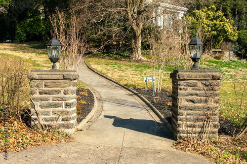 Two Cobblestone Pillars With Black Metal Lamps on Top With a Winding Path in the Background