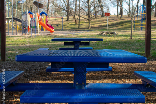 Blue Metal Benches in a Park in the shade with a playground in the background