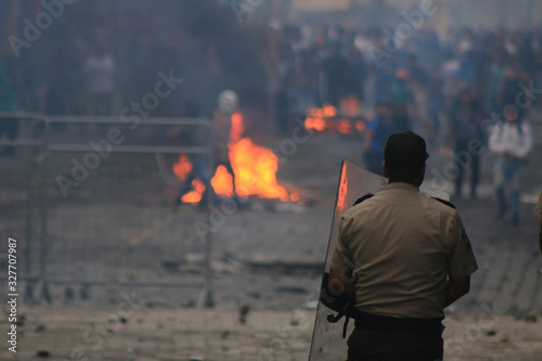 Photography A policeman waiting patiently at the other side of an angy mob