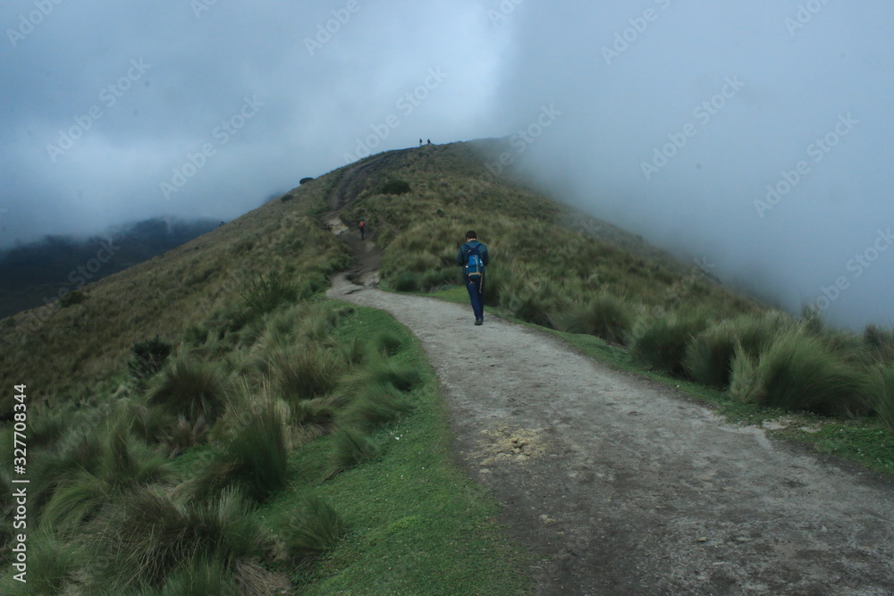 A lone hiker walking over a path in the Andes while fog is slowly covering the whole track