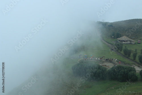 The fog is coming in from the edge of a cliff in de andes near quito, slowly covering the horse stable, path and house