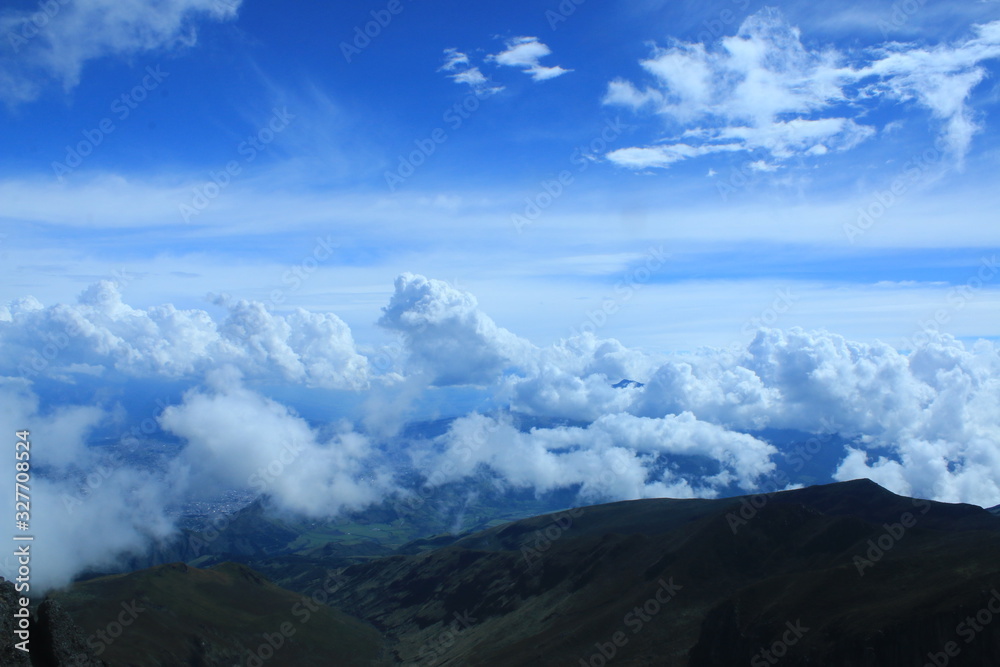 A beautiful cloudscape and birght blue colored sky against a dark mountain slope in the andes