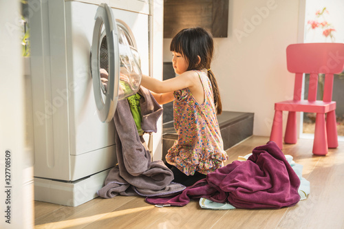 Canvas Print child girl little helper in laundry room near washing machine and dirty clothes