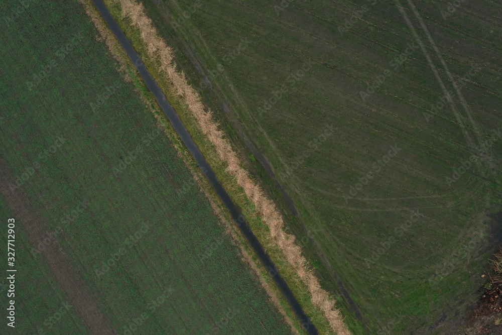 aerial view of an empty meadow with visible tracks from the tractor and a small hedge of reeds in the middle next to a small ditch