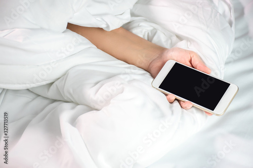 A woman lying in bed and holding a smartphone